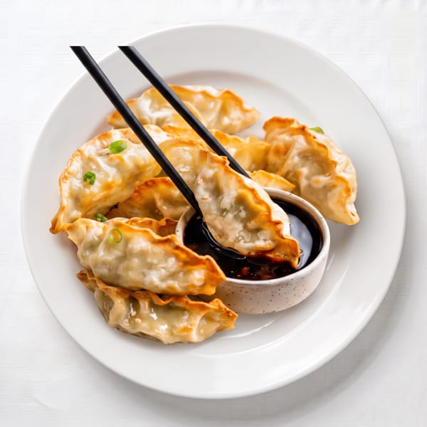 Golden-brown fried dumplings with green onions on a white plate, one dipped in soy sauce with chopsticks.