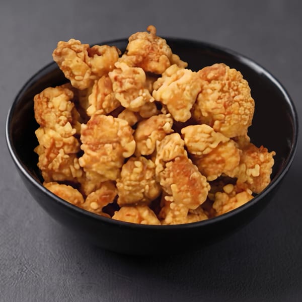 A black bowl filled with golden-brown, crispy fried popcorn chicken on a dark gray surface.