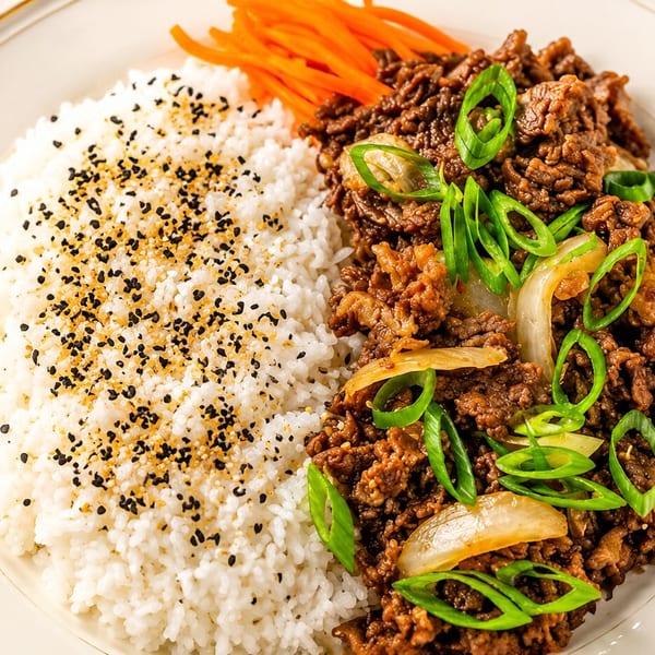 Bulgogi beef with white rice topped with sesame seeds and shredded carrots on a white plate.